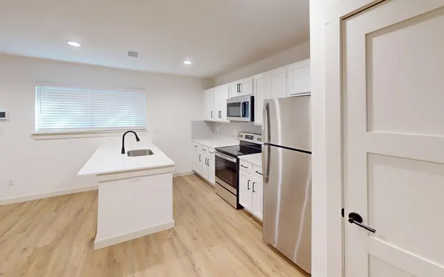A modern kitchen with white cabinetry, stainless steel appliances, and a countertop island with a sink.