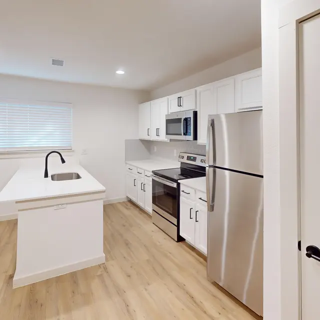 A modern kitchen with white cabinetry, stainless steel appliances, and a countertop island with a sink.
