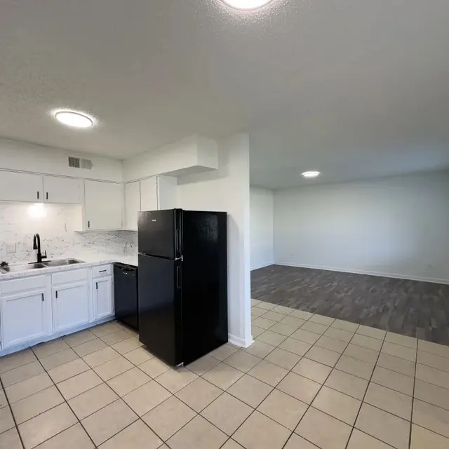 Spacious Modern Kitchen and Living Room View of a modern kitchen with black appliances and tiled floor, leading into a spacious living area with wooden flooring and natural light.