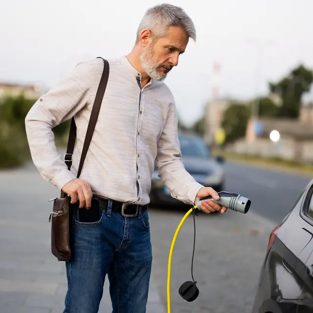 A man stands next to a car, holding a charging cable while preparing to charge an electric vehicle.