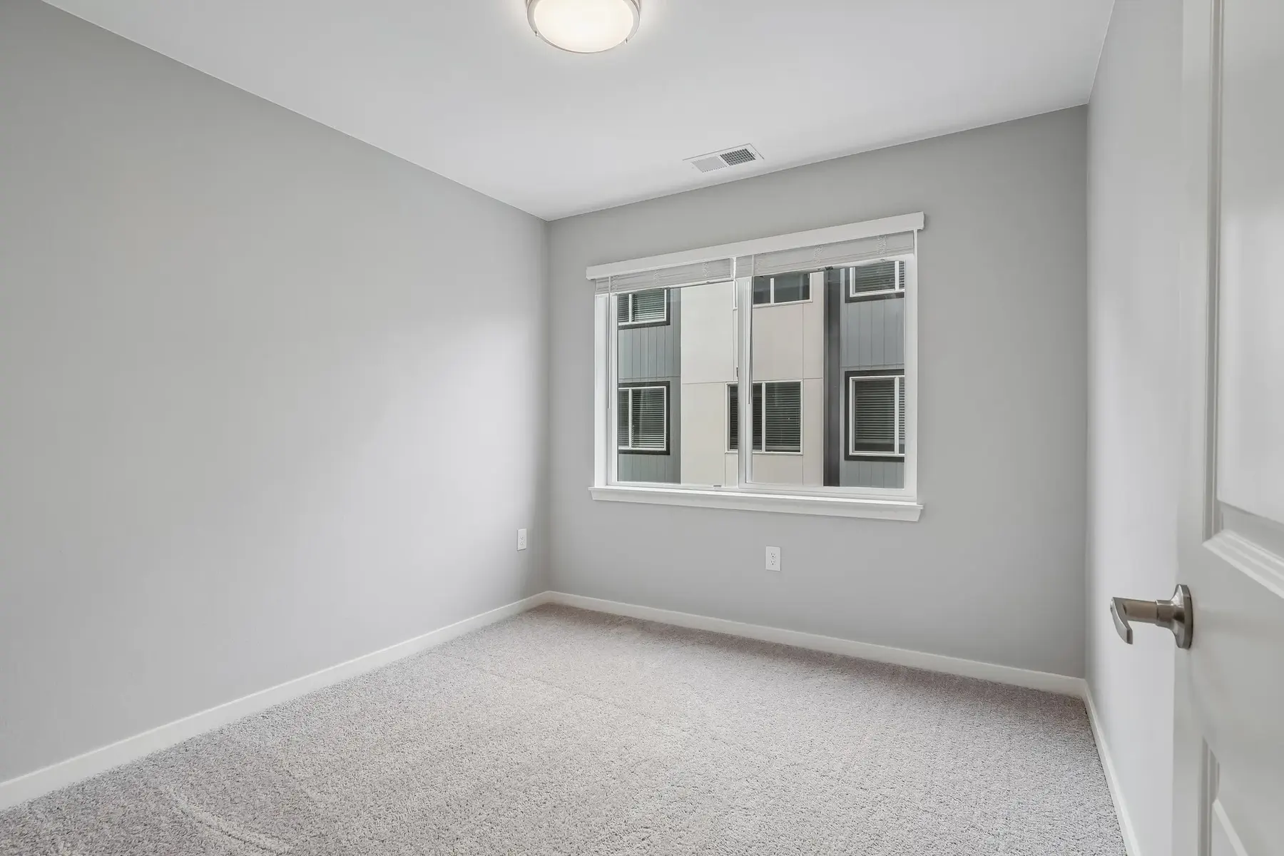 Vacant Bedroom with Gray Walls A vacant bedroom featuring gray walls and carpet, with a window overlooking a building facade.