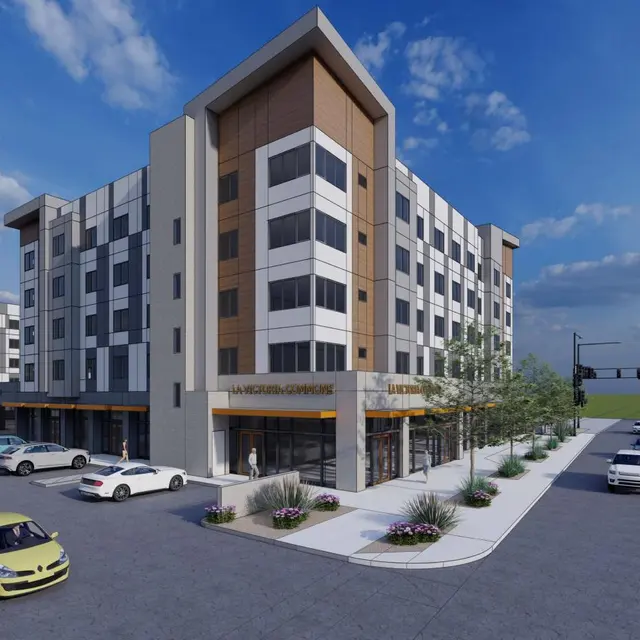 A modern apartment building with a contemporary architectural design, featuring multiple stories, a mix of light and dark colored panels, and surrounded by landscaped areas.