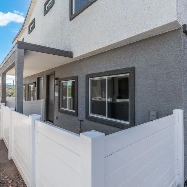 Modern Townhouse Exterior Exterior view of a modern townhouse with a fenced patio area, featuring white wooden fencing and a grey exterior.