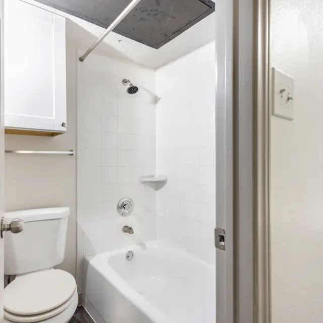 A small bathroom featuring a white bathtub with a showerhead, a toilet, and a light-colored cabinet on the wall.