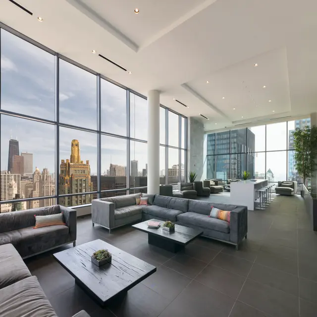 A modern lounge area featuring multiple gray sofas and stylish coffee tables, with large windows providing a panoramic view of a city skyline.