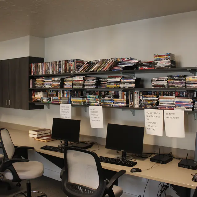A library interior featuring a row of computers and shelves filled with DVDs.