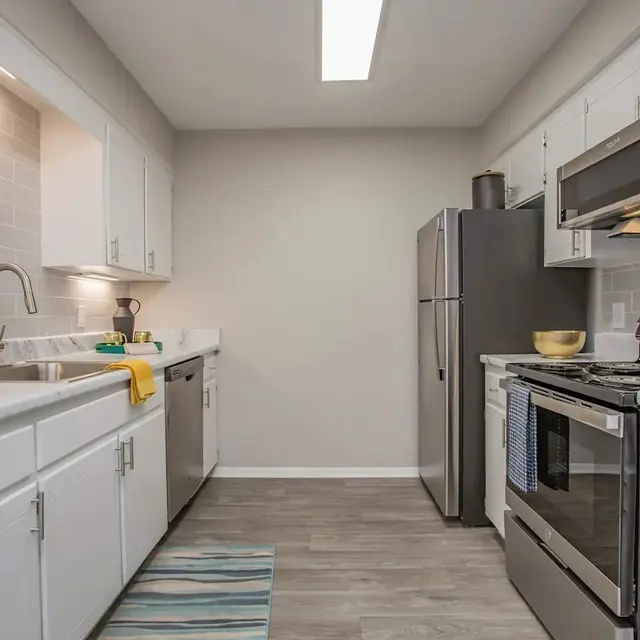 Modern kitchen featuring white cabinets, stainless steel appliances, a dishwasher, and a gray backsplash. Bright and spacious layout.