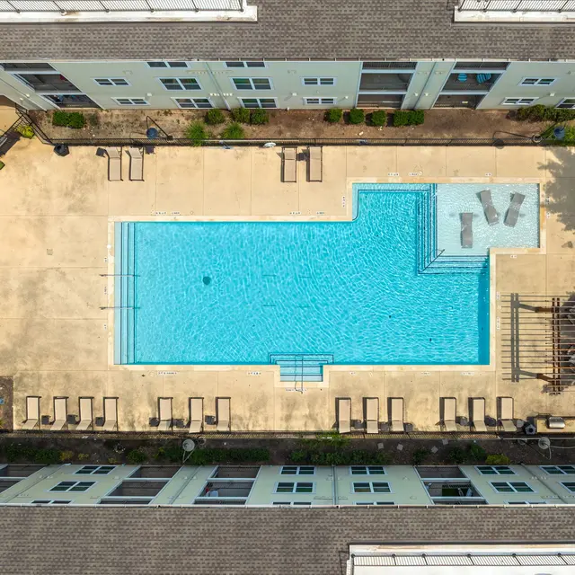 Aerial view of a large swimming pool surrounded by lounge chairs and apartment buildings.