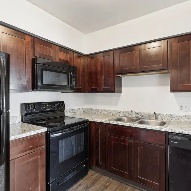 A modern kitchen featuring dark wood cabinetry, black appliances, and granite countertops.