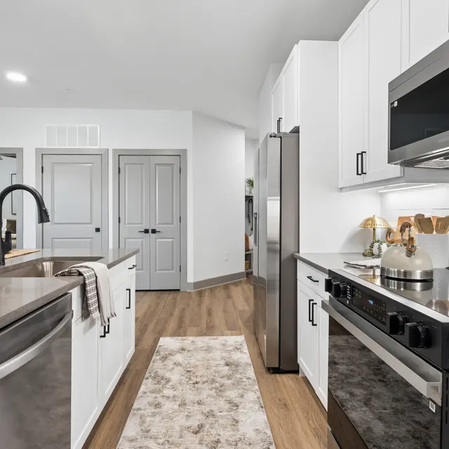 Stylish Modern Kitchen A stylish kitchen featuring white cabinetry, stainless steel appliances, and modern fixtures. The layout includes a central island with a countertop and a decorative rug on wooden flooring.