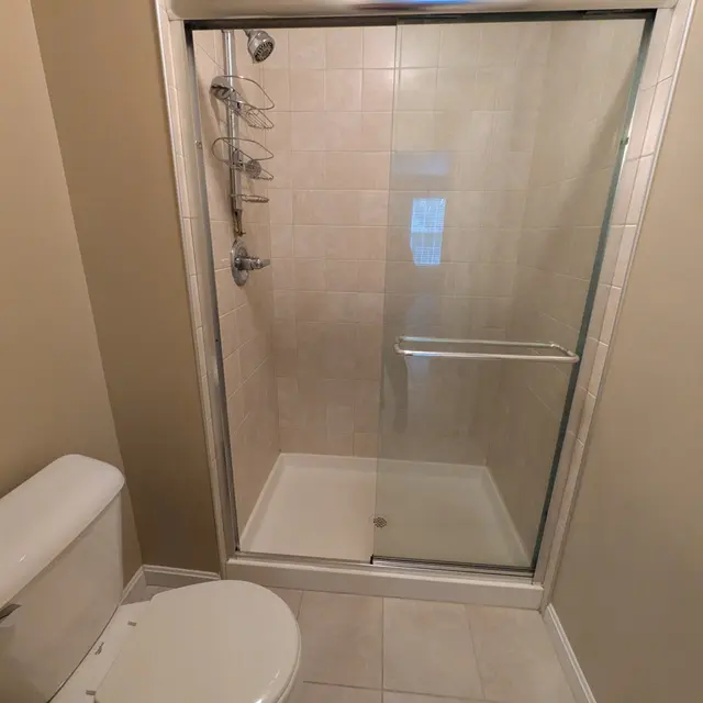 A clean bathroom featuring a glass shower enclosure, a toilet, and tiled flooring.