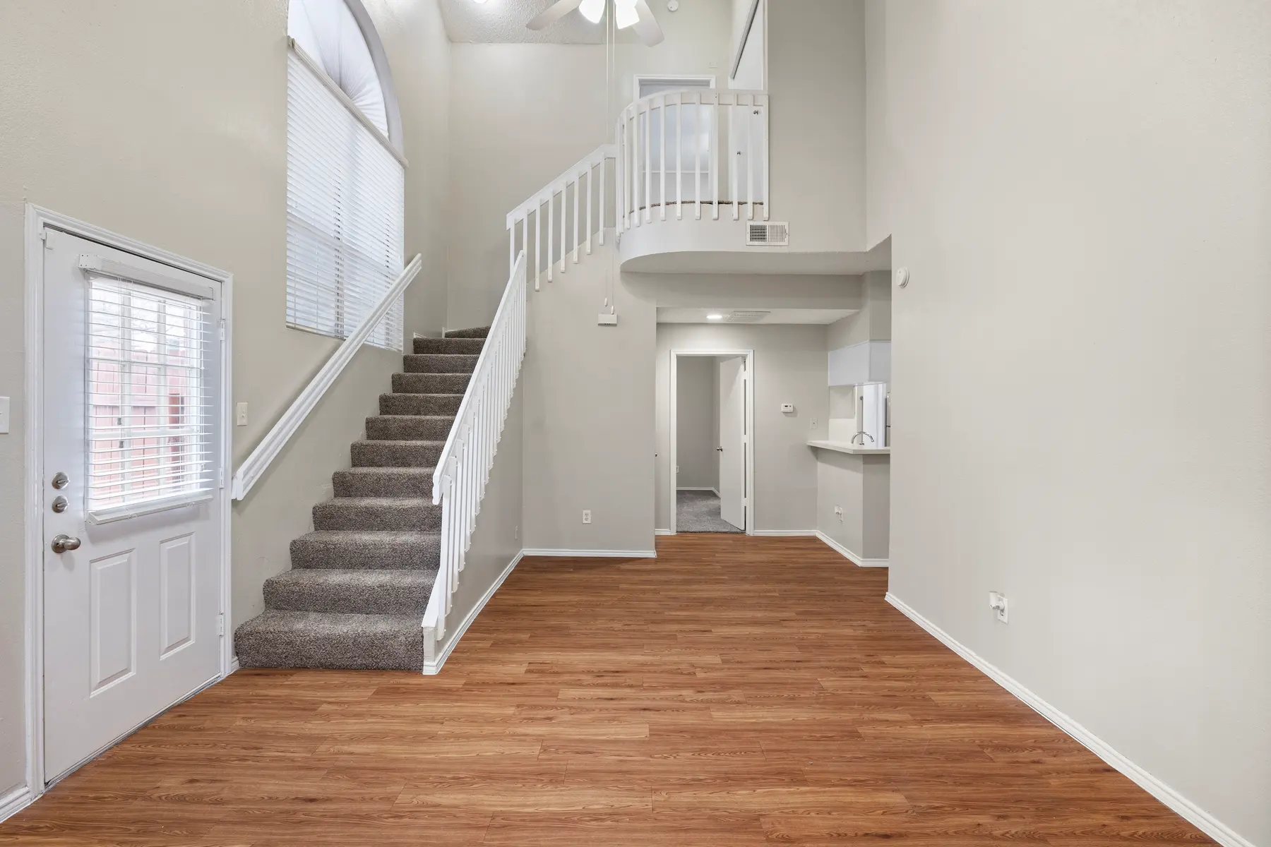 A modern, spacious living area featuring a staircase, large windows, and wooden flooring.