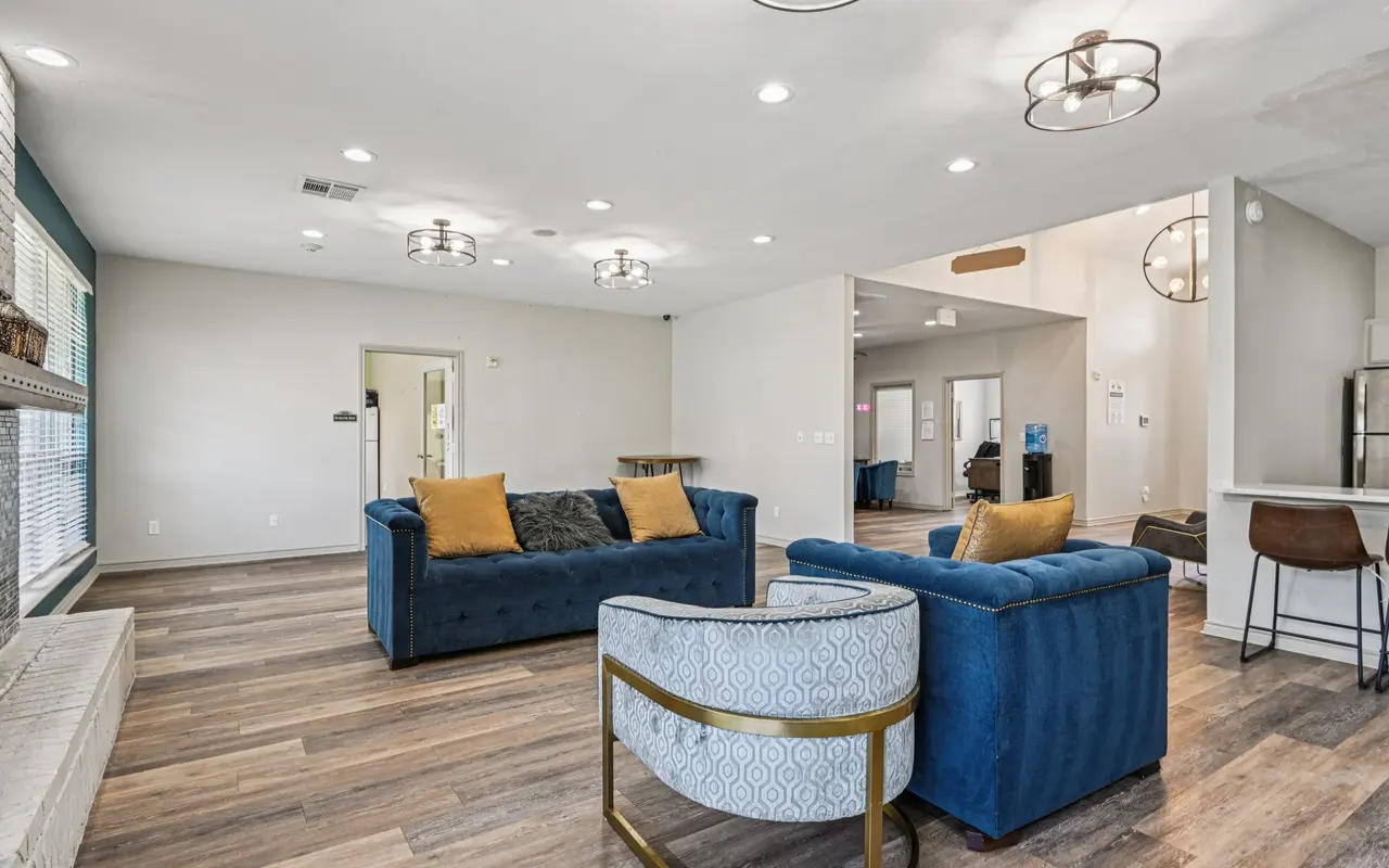 A modern living room featuring two blue sofas, a round patterned chair, large windows letting in natural light, and pendant lighting fixtures on the ceiling.