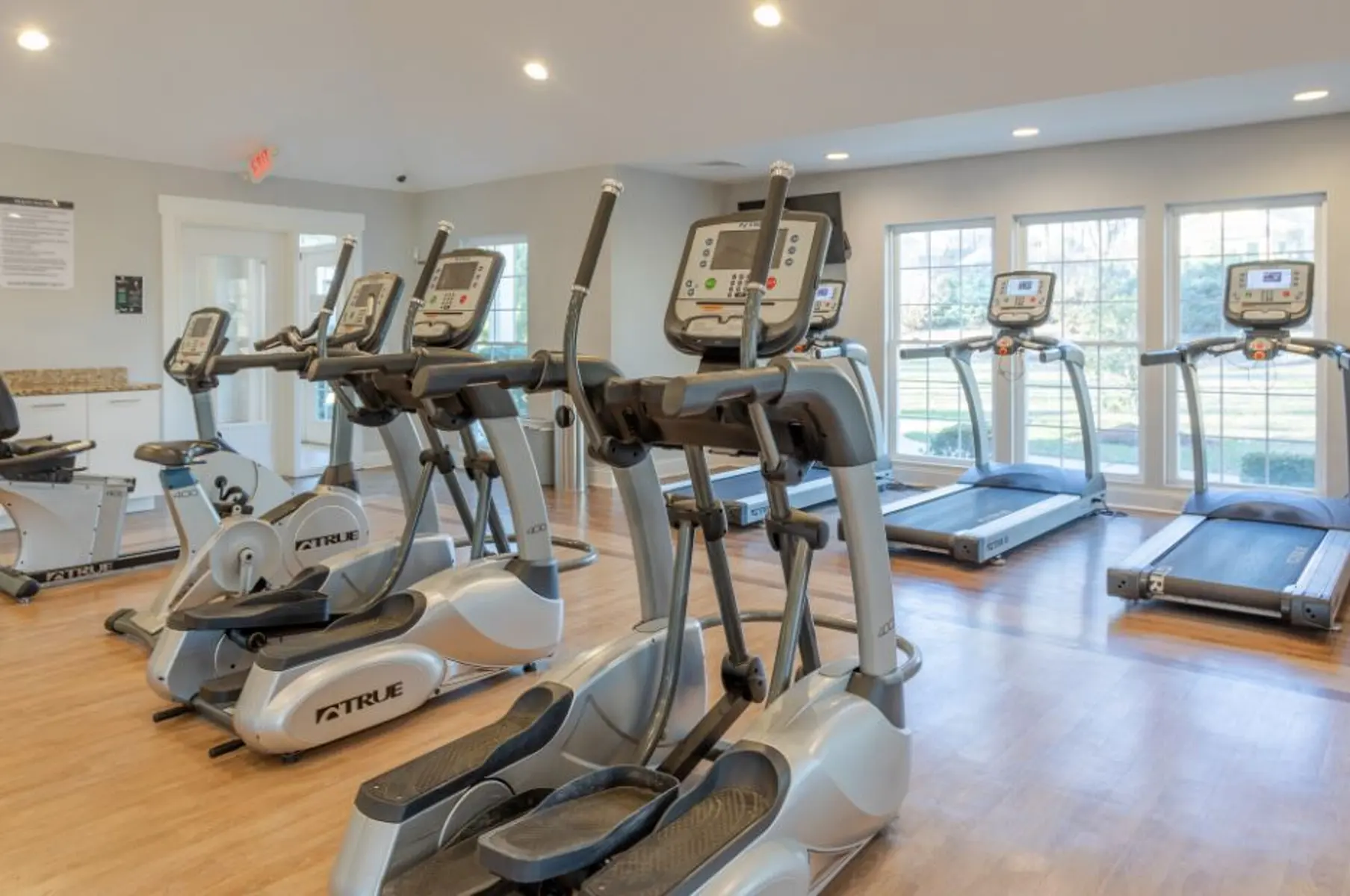 Interior view of a fitness center showing elliptical machines and treadmills with large windows allowing natural light.