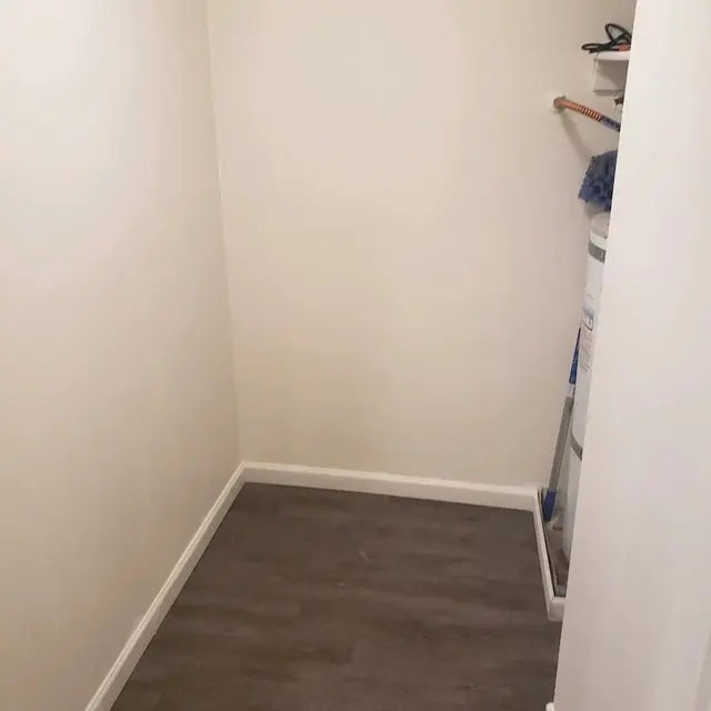 An empty small storage room with light-colored walls and brown laminate flooring.