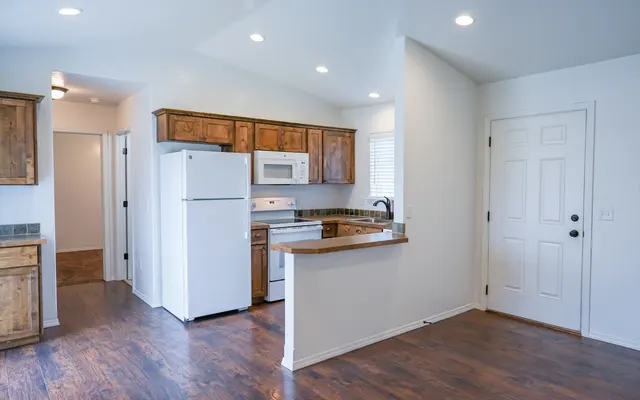 Modern Kitchen Interior A modern kitchen with wooden cabinetry, a white refrigerator, microwave, and stove, featuring light-colored walls and a door leading outside.
