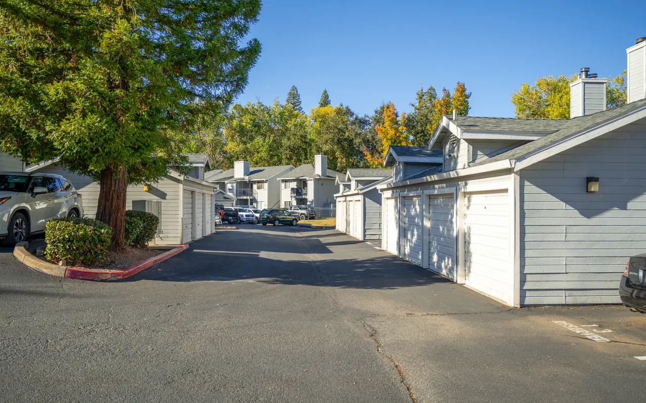 A driveway leading through an apartment complex with garages on either side and trees in the background.