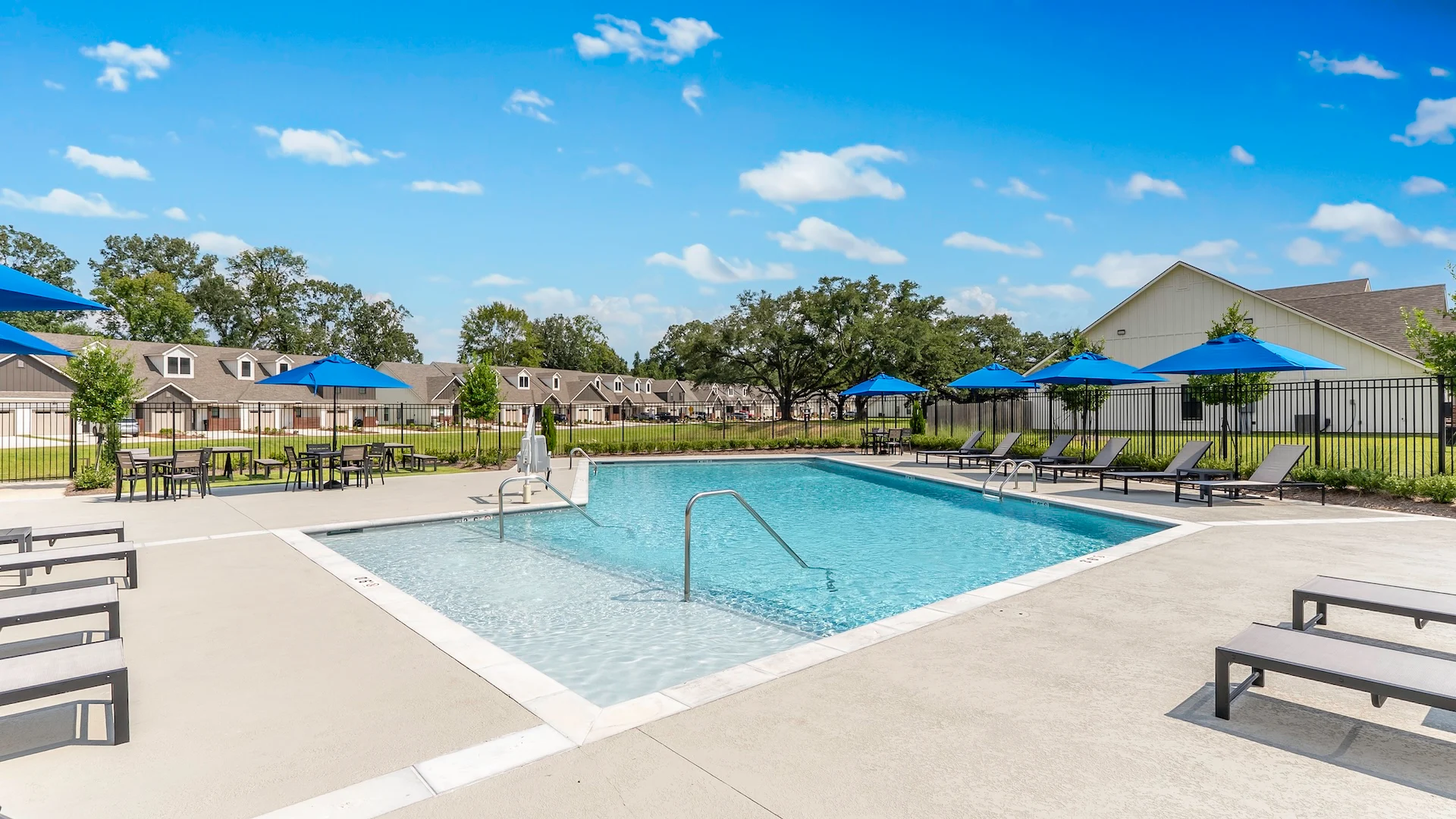 Sunny Swimming Pool Area A swimming pool area with lounge chairs and blue umbrellas under a clear sky.