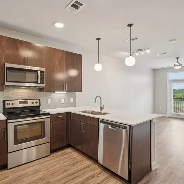A modern kitchen featuring dark wood cabinetry, stainless steel appliances, and a spacious open layout leading to a living area with large windows.