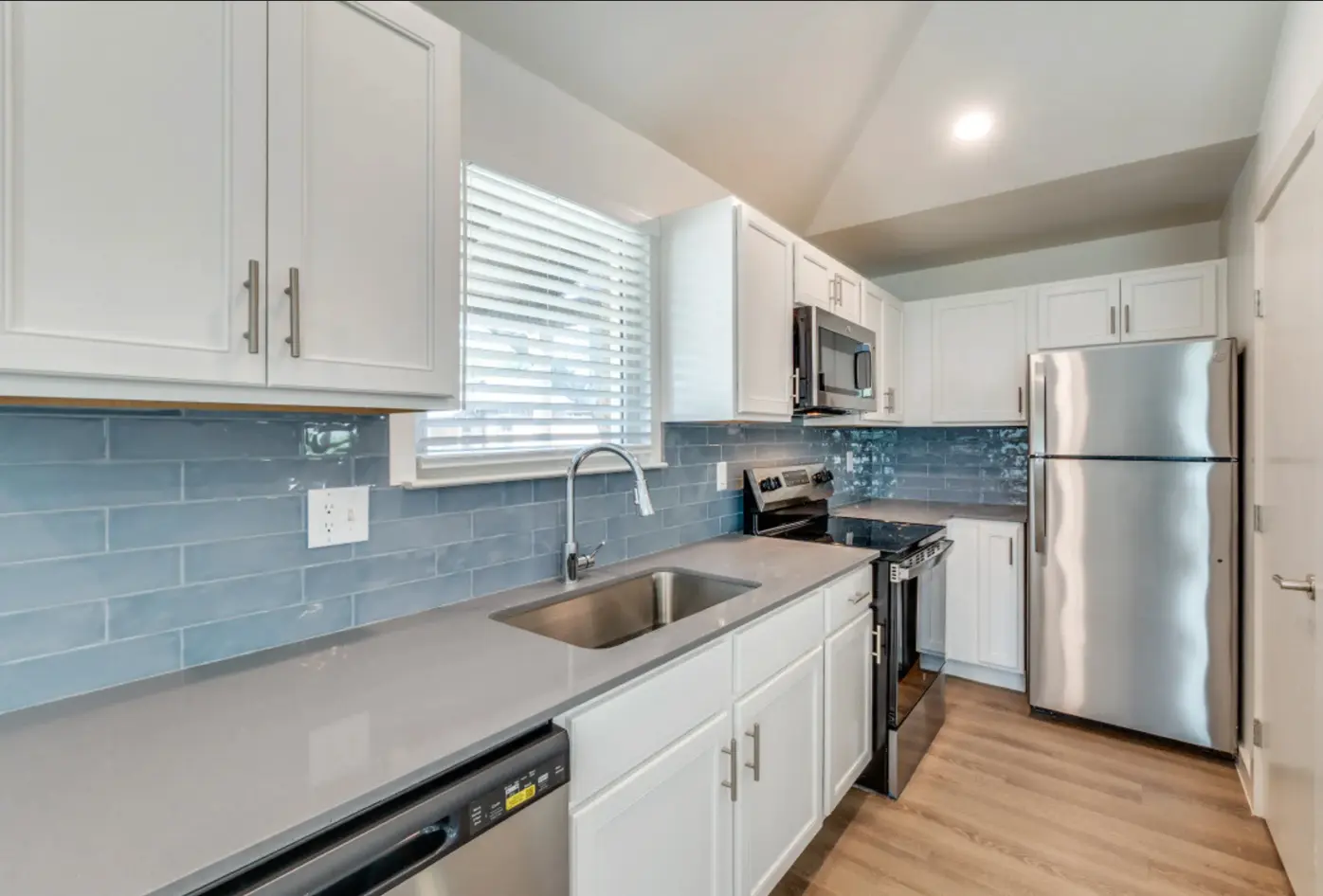 Modern kitchen with gray and white cabinetry, stainless steel appliances, and blue tile backsplash.