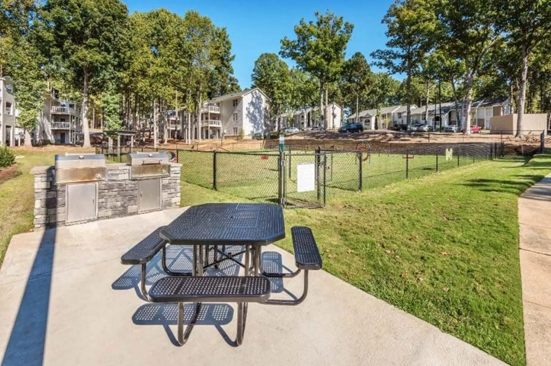 Outdoor picnic area with a black table and grill units in an apartment complex setting.