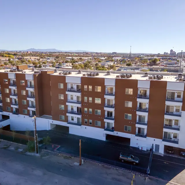 Aerial view of a modern apartment building with a brown and white facade, surrounded by a residential area and roads.