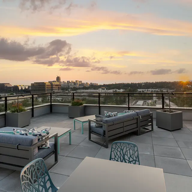 Stunning Rooftop Sunset View A modern rooftop terrace featuring stylish outdoor furniture with a scenic view of a city skyline during sunset. Soft orange and purple hues fill the sky as the sun sets in the background.