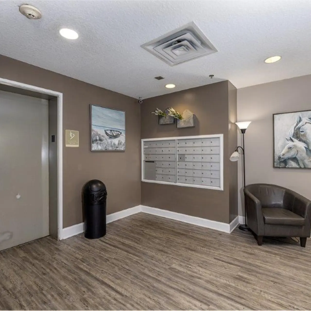 Interior view of a lobby area featuring an elevator, mailboxes, a chair, and wall decor.