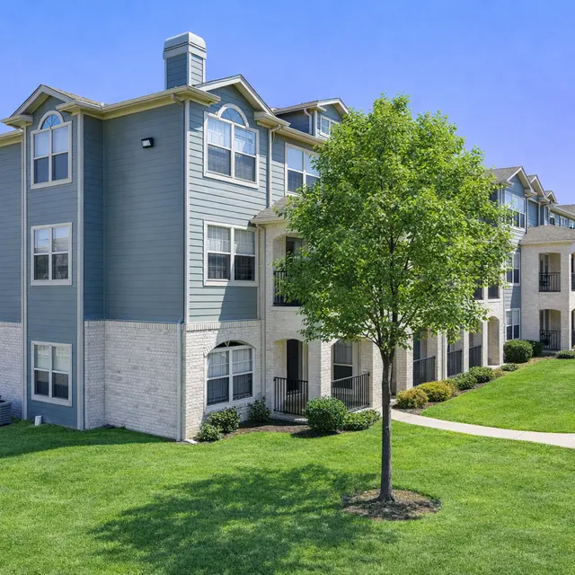 Modern Apartment Complex with Green Landscaping A well-maintained apartment complex featuring multiple stories, with a green lawn and trees in front.