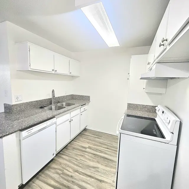 A modern kitchen featuring white cabinets, granite countertops, and stainless steel appliances. The kitchen has a spacious feel with natural lighting from a ceiling window.