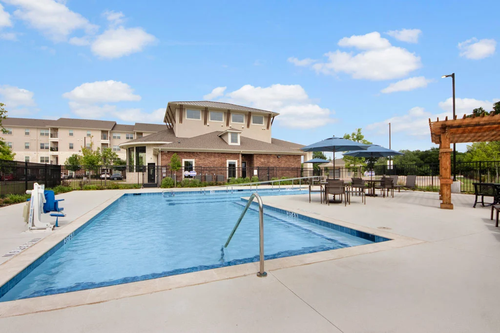 Inviting Community Pool Space An outdoor swimming pool area with a brick building in the background, surrounded by lounge chairs and umbrellas.