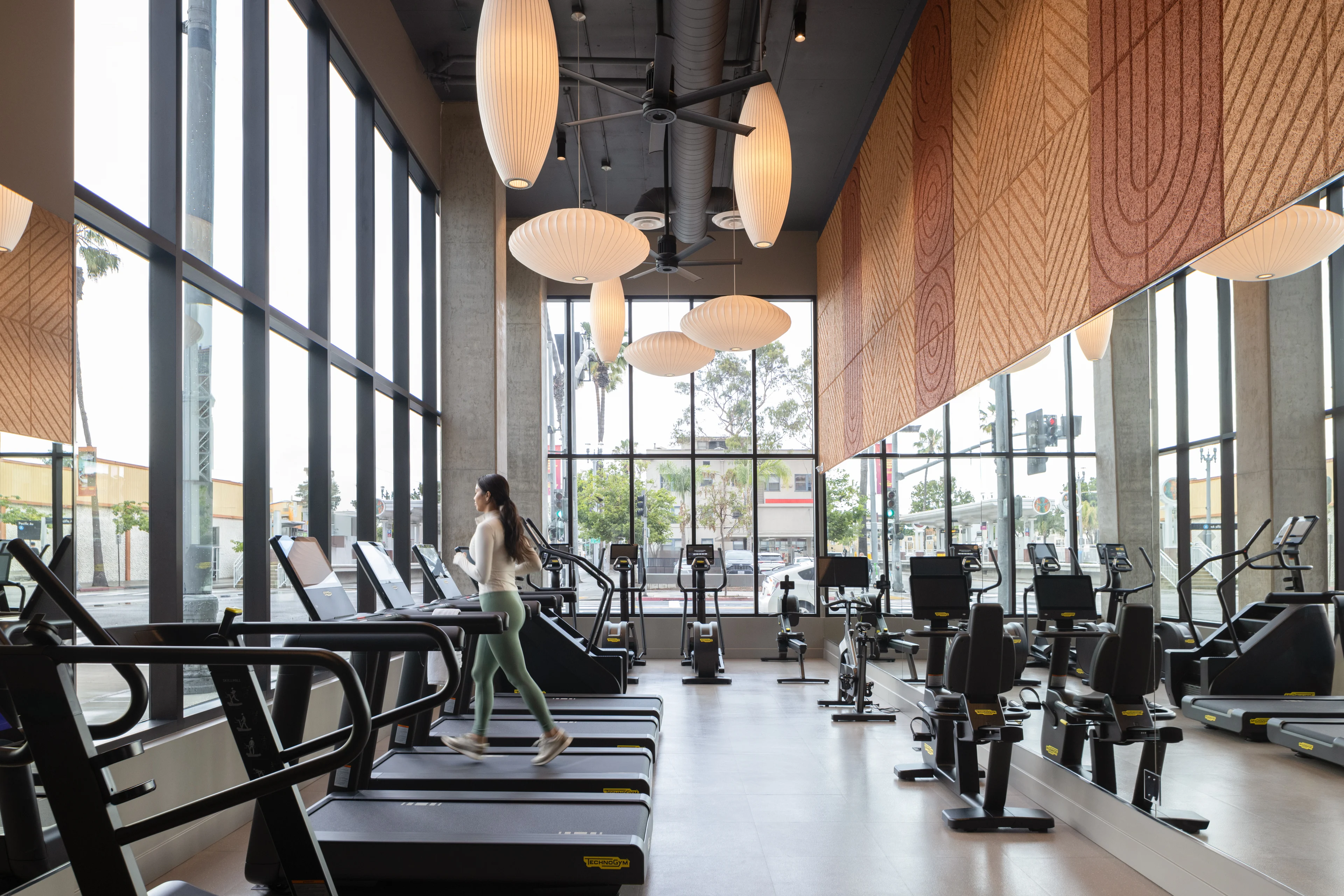 Modern Gym Interior A modern gym interior featuring large windows, several treadmills, and elliptical machines, with a person jogging on a treadmill.
