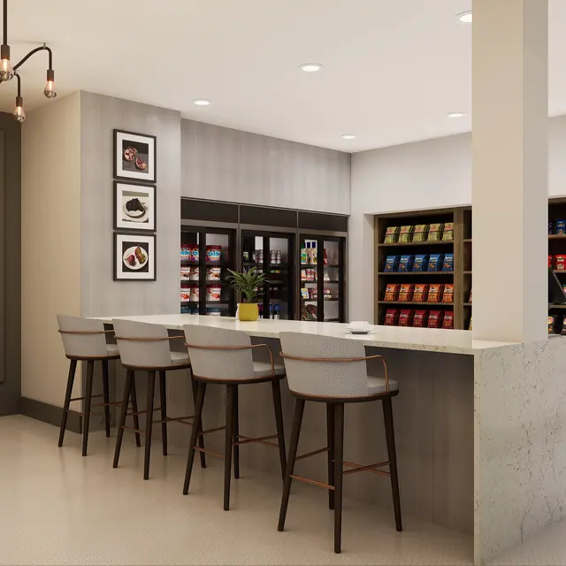 A contemporary kitchen interior featuring a long bar with stools, stylish lighting, and shelves filled with various packaged goods.