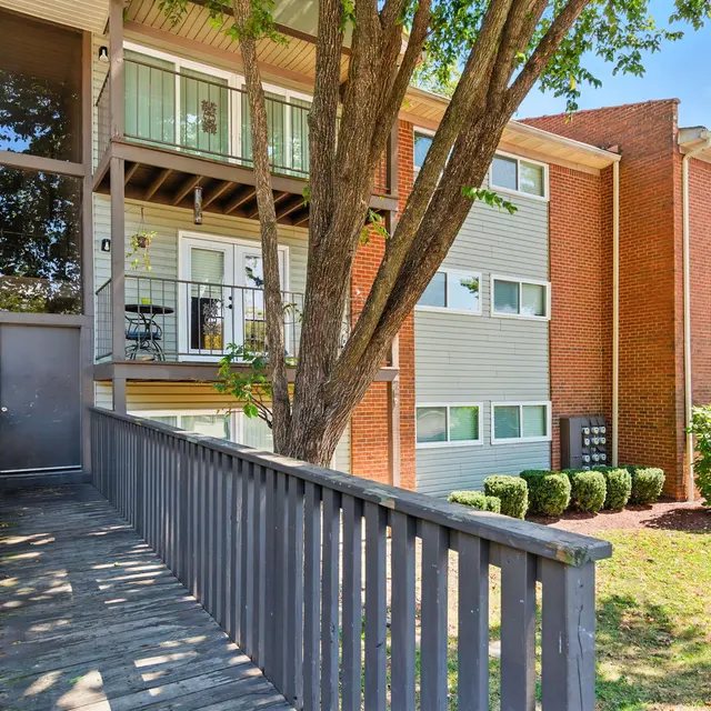 Exterior view of a three-story apartment building featuring balconies and a wooden walkway entry.
