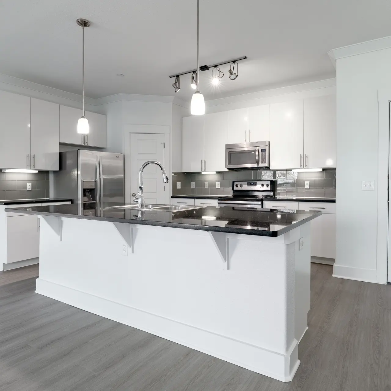 A spacious modern kitchen featuring white cabinetry, stainless steel appliances, and a large countertop with a sleek design.