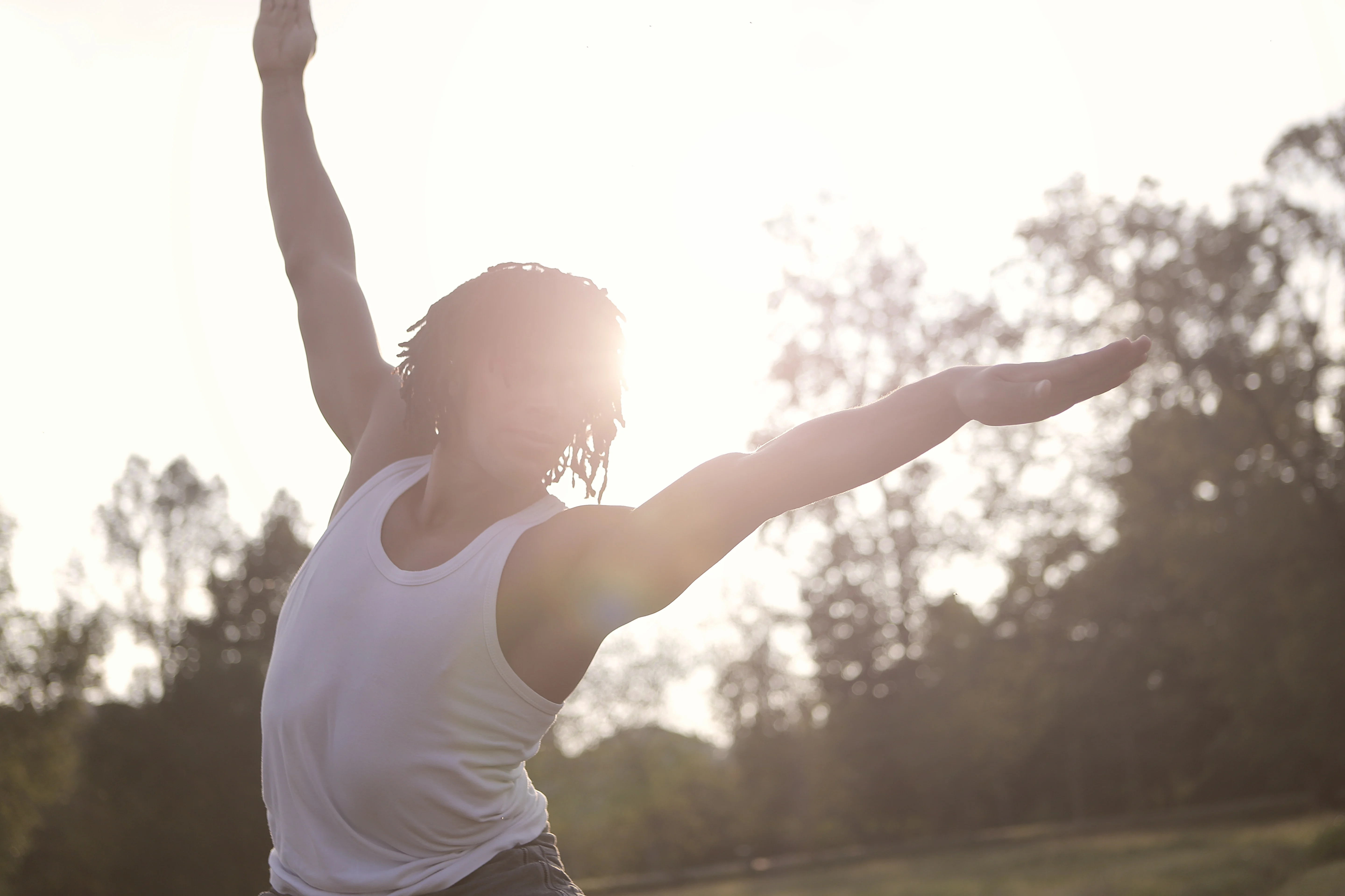 Dancer in Nature A dancer poses in a sunlit outdoor setting, arms outstretched, with the sun casting a glow behind them.