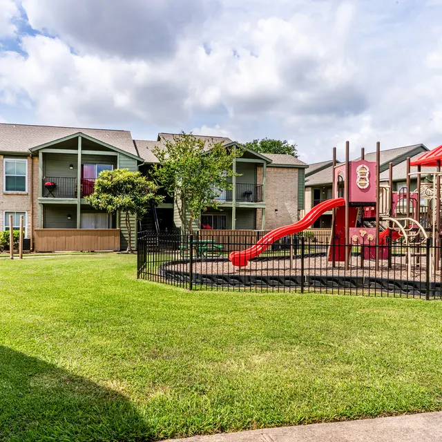 Playground area in front of an apartment complex with grassy lawn and cloudy sky
