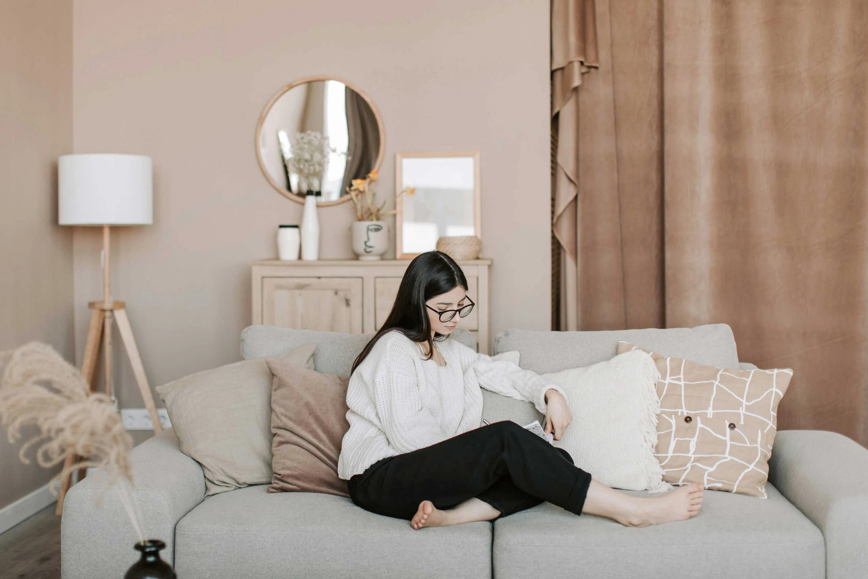 Cozy Living Room Scene A woman sitting on a grey sofa in a cozy living room, surrounded by cushions and decor.
