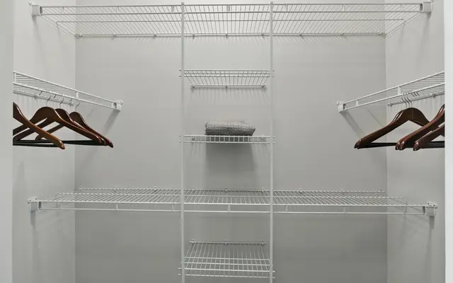 Empty closet with wire shelves and wooden hangers, featuring a gray folded item on the middle shelf.