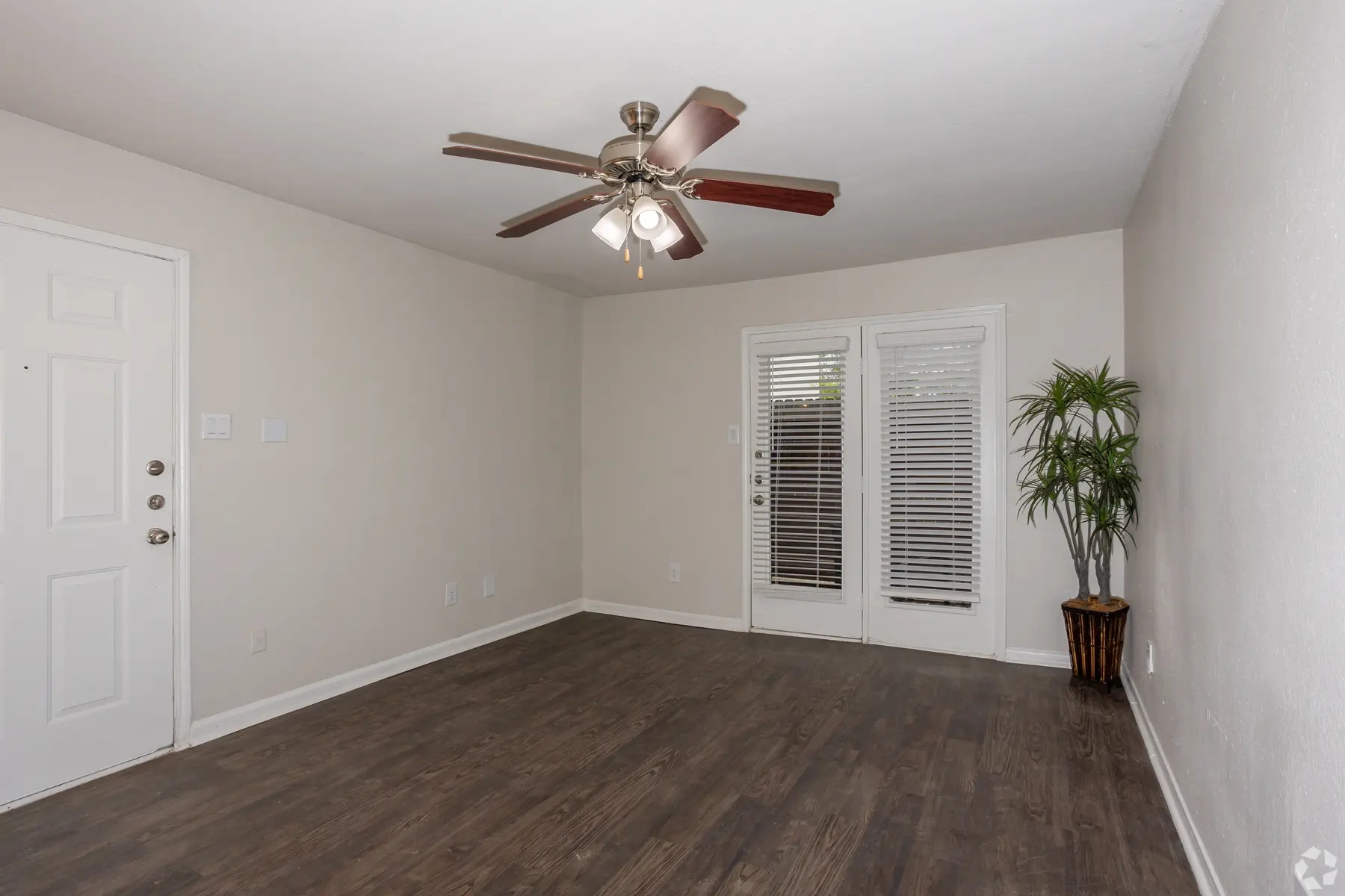 Spacious Empty Living Room A spacious empty living room with a ceiling fan, a door, and sliding glass doors leading outside. A potted plant is placed in the corner.