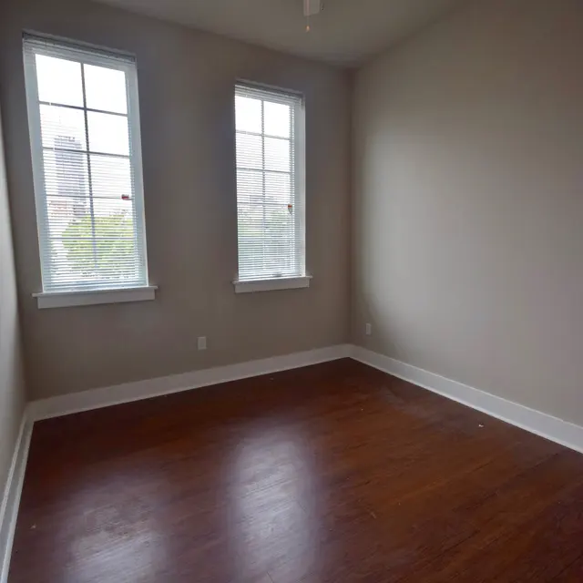 Spacious Empty Room with Windows A small empty room featuring two windows, a ceiling fan, and hardwood flooring.