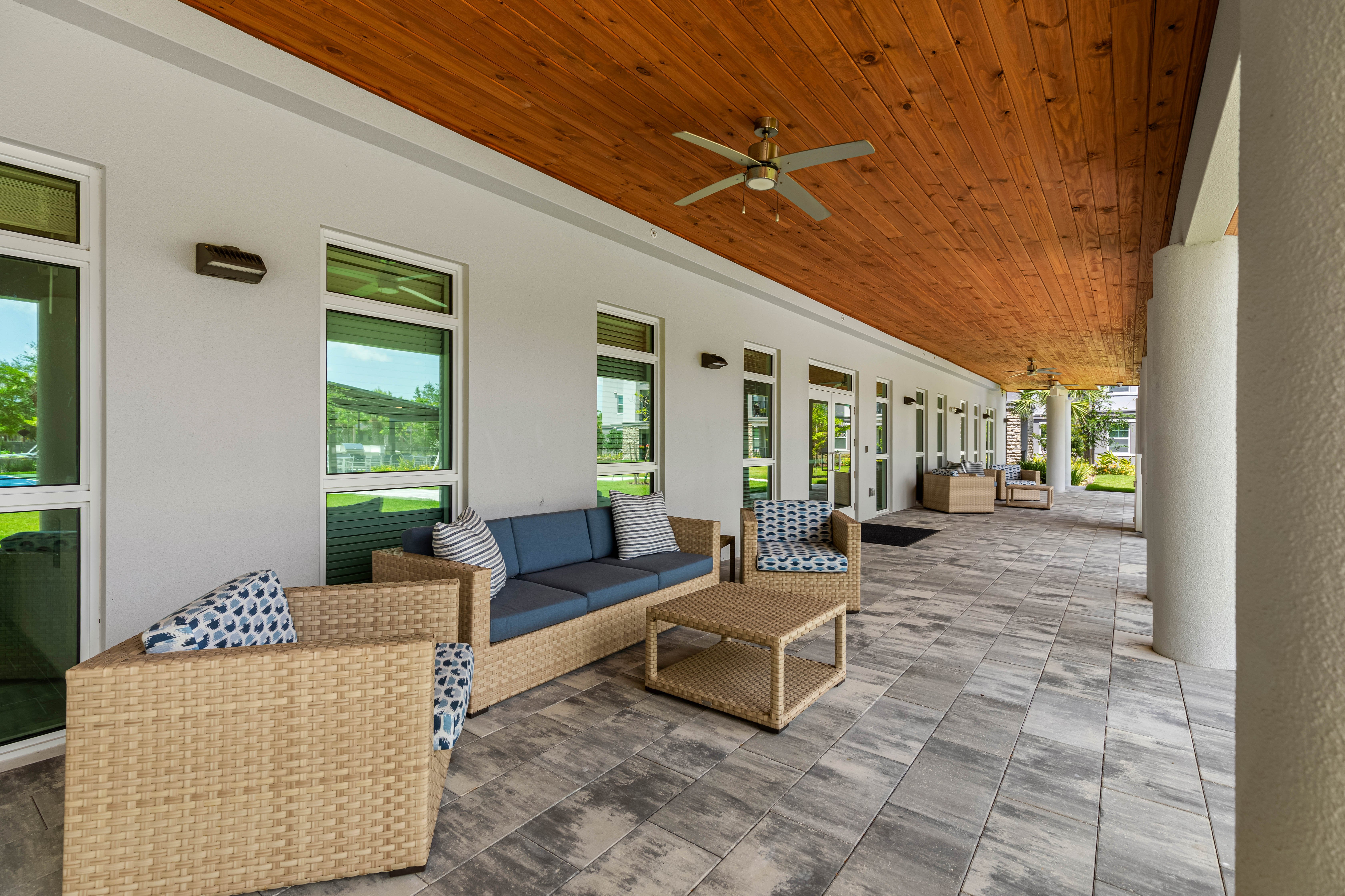 A spacious outdoor lounge area featuring wicker furniture, including couches and a coffee table under a wooden ceiling.
