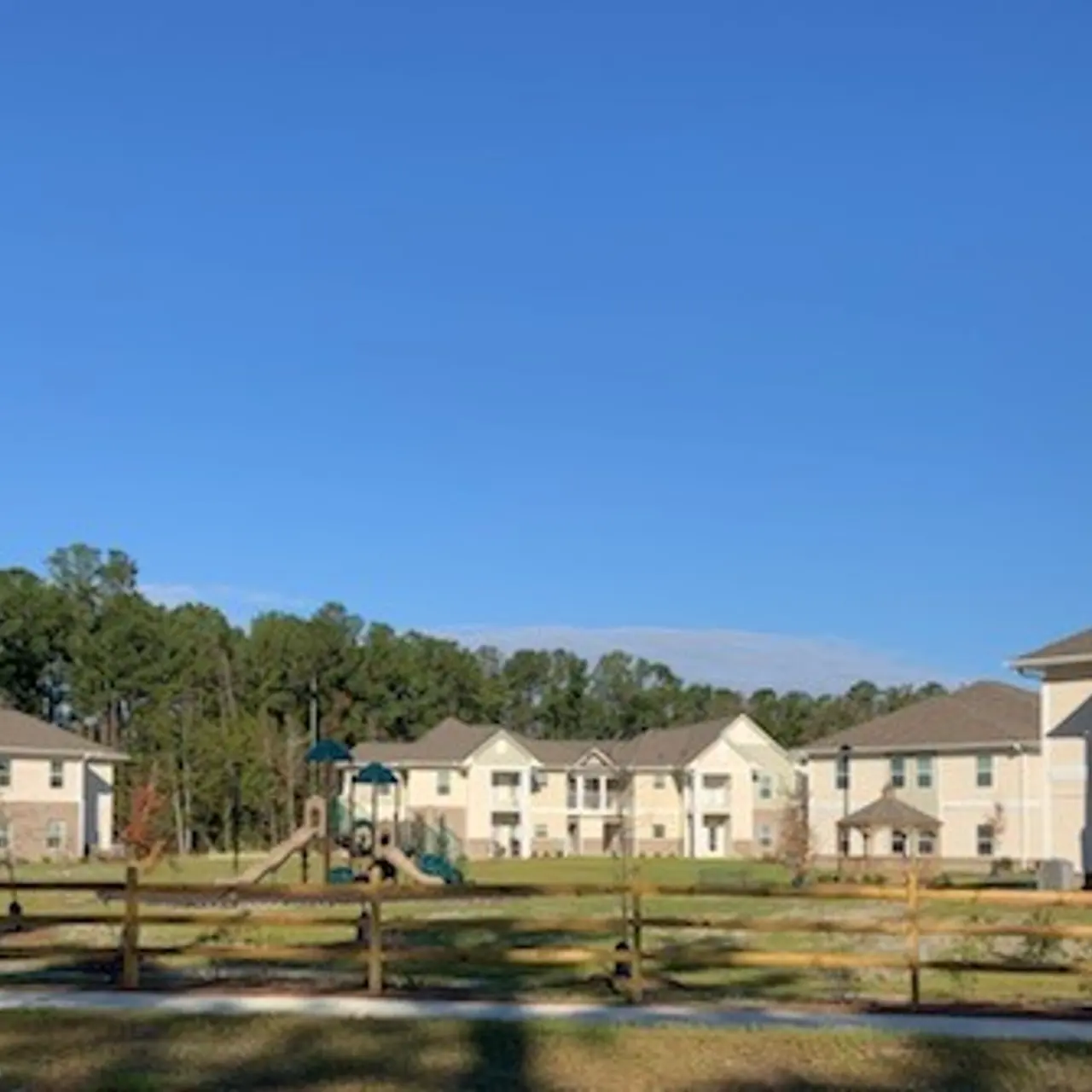View of an apartment complex with four buildings, a playground in the center, and a wooden fence.