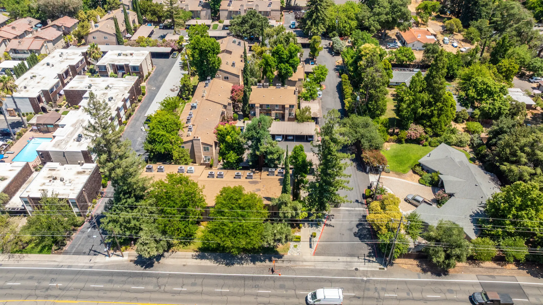Aerial view of a suburban neighborhood featuring various residential buildings, trees, and a swimming pool area.