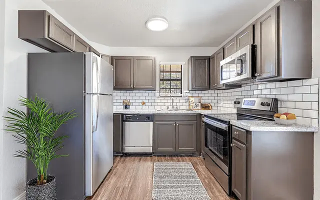 A modern kitchen featuring gray cabinets, stainless steel appliances, and a small potted plant in the corner. The countertop is light-colored with a stylish backsplash of white tiles.