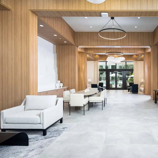 A spacious modern lobby with wooden paneling, featuring stylish furniture, artistic wall decor, and ample natural light from large windows.