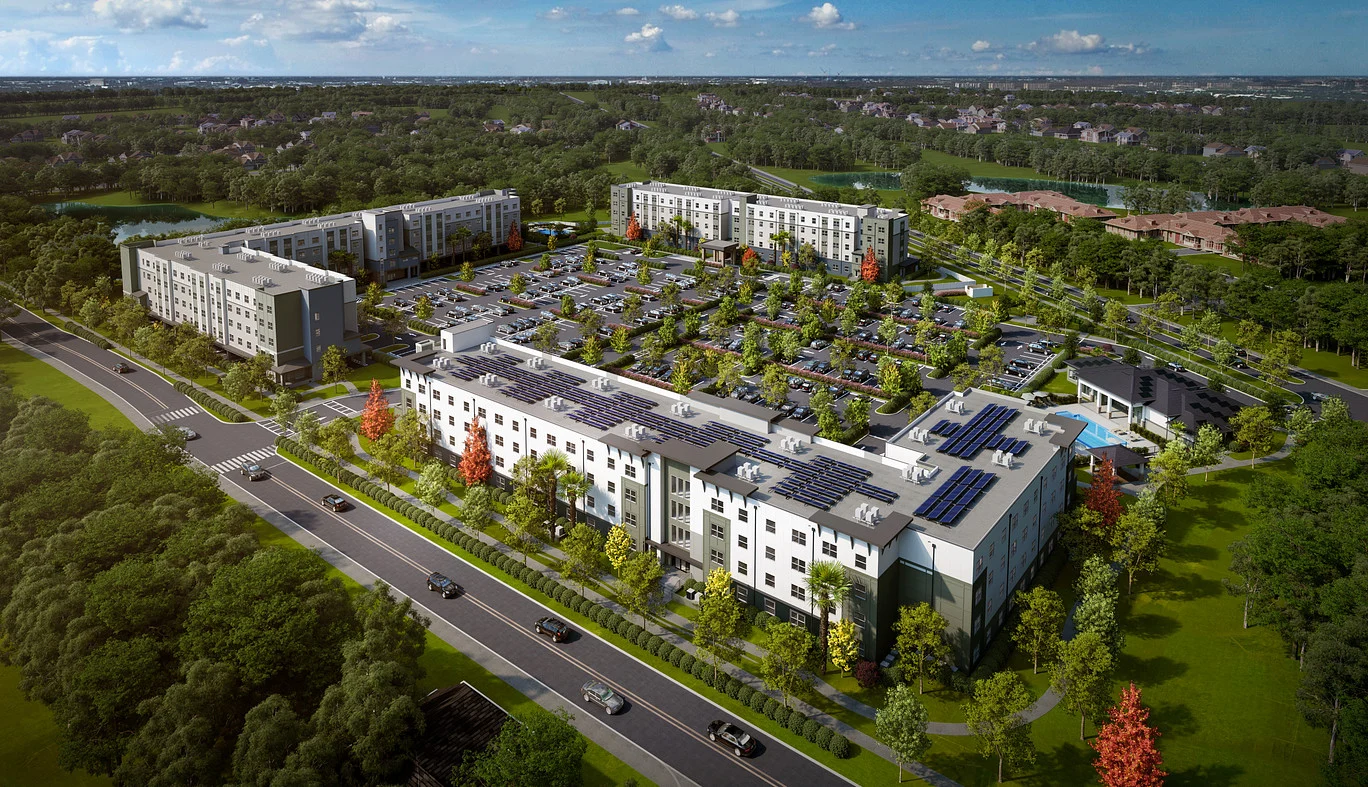 Aerial view of a modern apartment complex surrounded by greenery, featuring multiple buildings, parking lots, and solar panels on roofs.