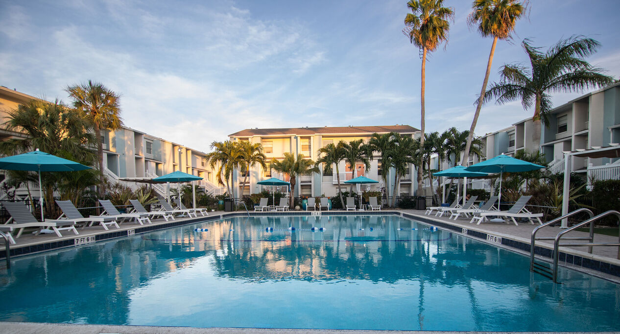 A beautiful swimming pool area surrounded by palm trees and lounge chairs with turquoise umbrellas on a sunny day.