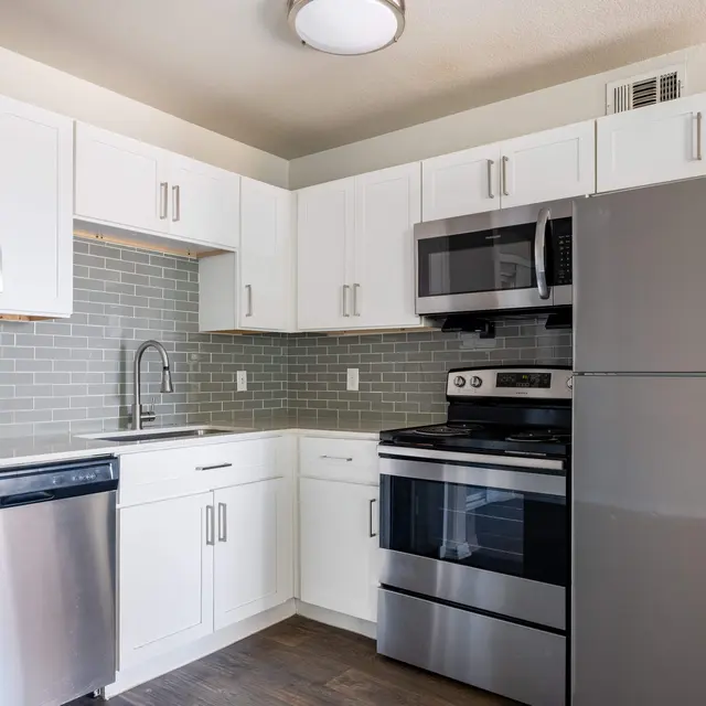 A modern kitchen featuring white cabinets, stainless steel appliances including a refrigerator, stove, and dishwasher, and a modern backsplash with gray tiles.