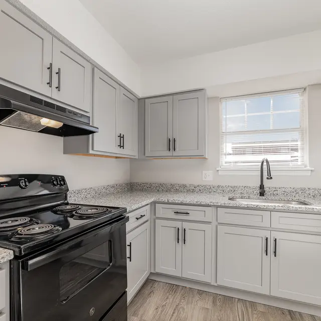 A modern kitchen featuring gray cabinets, a black stove, and a sink under a window.